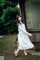 A woman standing in front of a house wearing a blue and white dress.